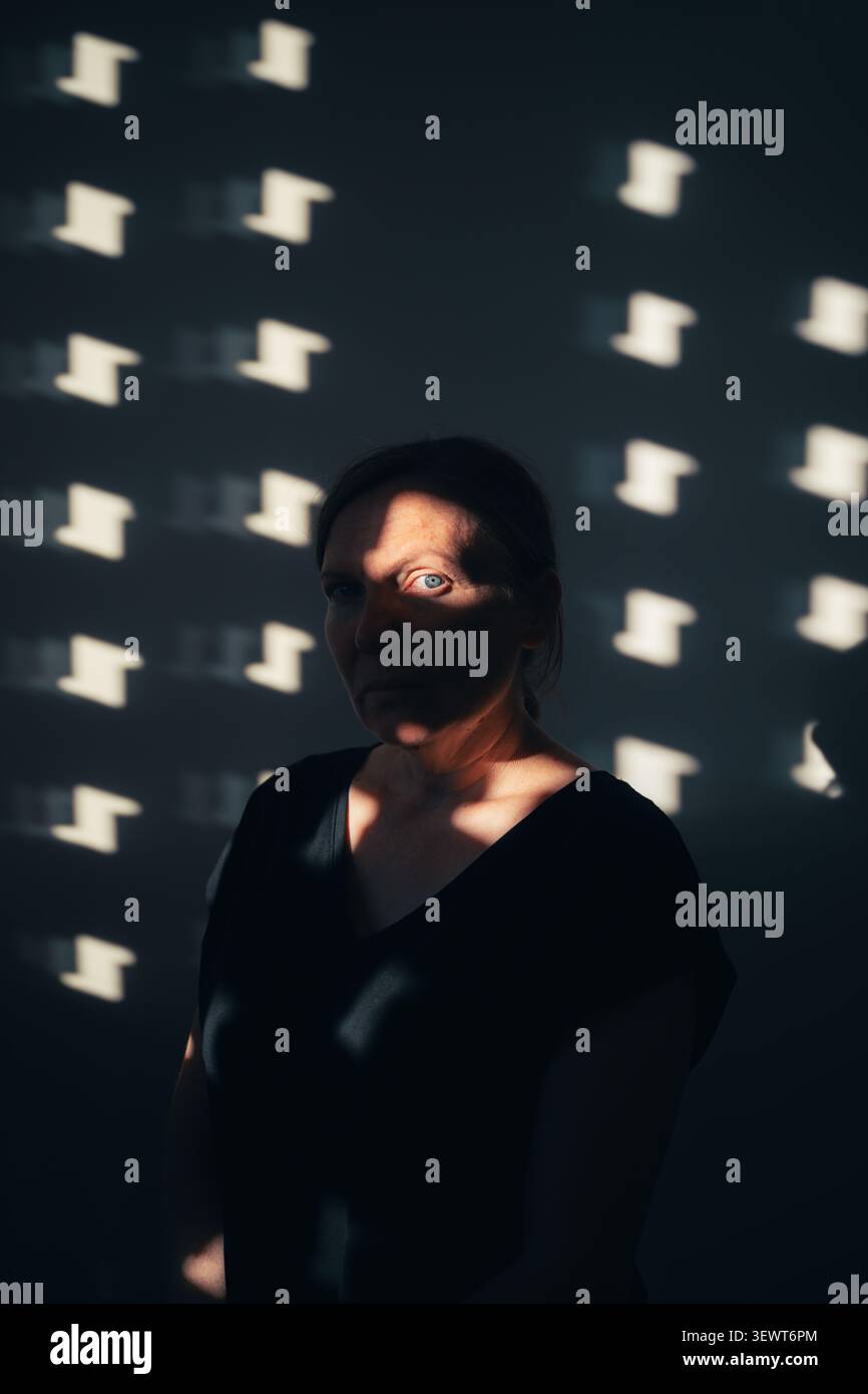 Ritratto di una donna parzialmente illuminata dalla luce solare e dall'ombra. Concetto di mistero, identità, introspezione e complessità emotiva. Sele Foto Stock