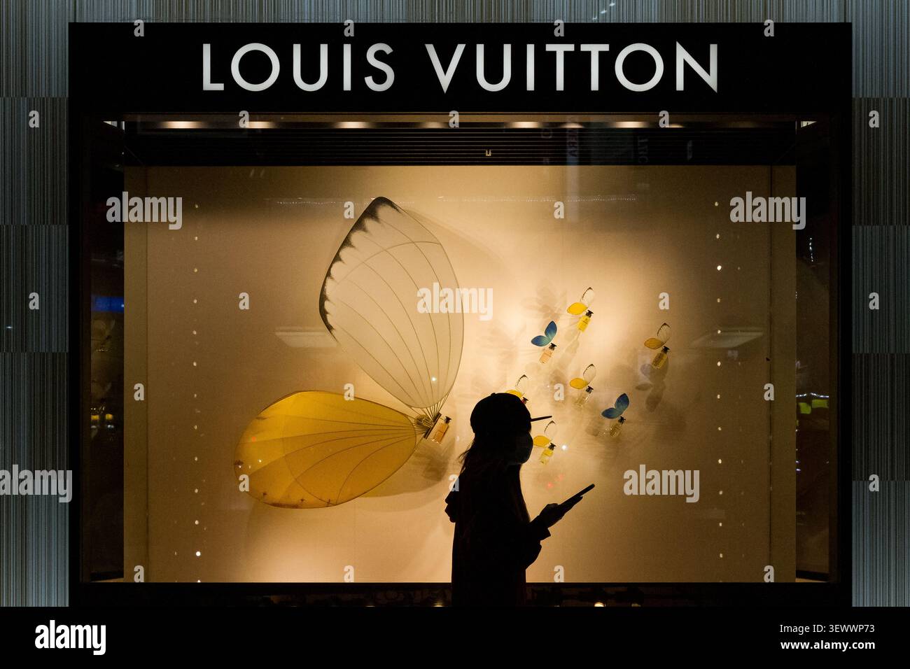 Una donna che usa uno smartphone, passa davanti a una vetrina di Louis Vuitton a Ikebukero, Tokyo, Giappone. Foto Stock