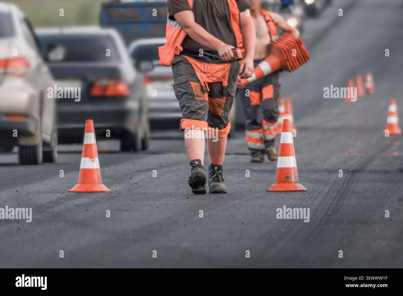 Lavoratori stradali che collocano coni stradali durante la riparazione di strade asfaltate su strade trafficate. Concetto di chiusura corsia, manutenzione stradale, controllo del traffico, const Foto Stock