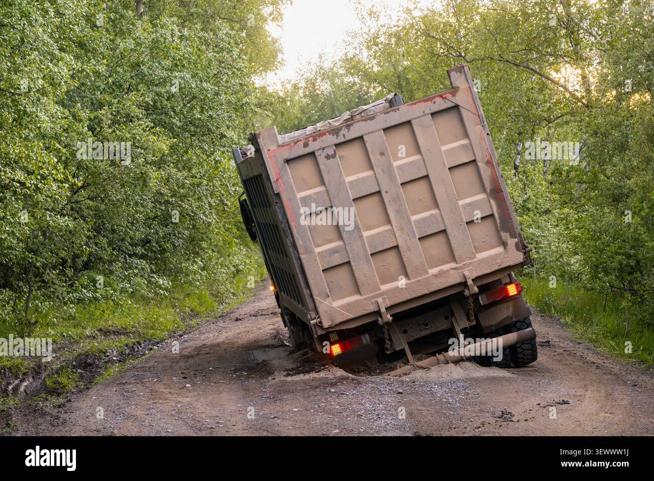Dumper pesante inclinato dopo essere rimasto bloccato su una strada sterrata danneggiata in una foresta. Concetto di cattive condizioni stradali, trasporto fuoristrada, costruzione, basso Foto Stock