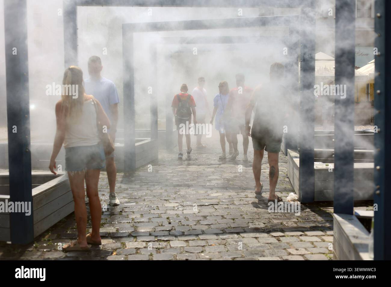 Durante l'ondata di caldo del giugno 2026 a Budapest, in Ungheria, le persone si godono la nebbia rinfrescante all'aperto per strada Foto Stock