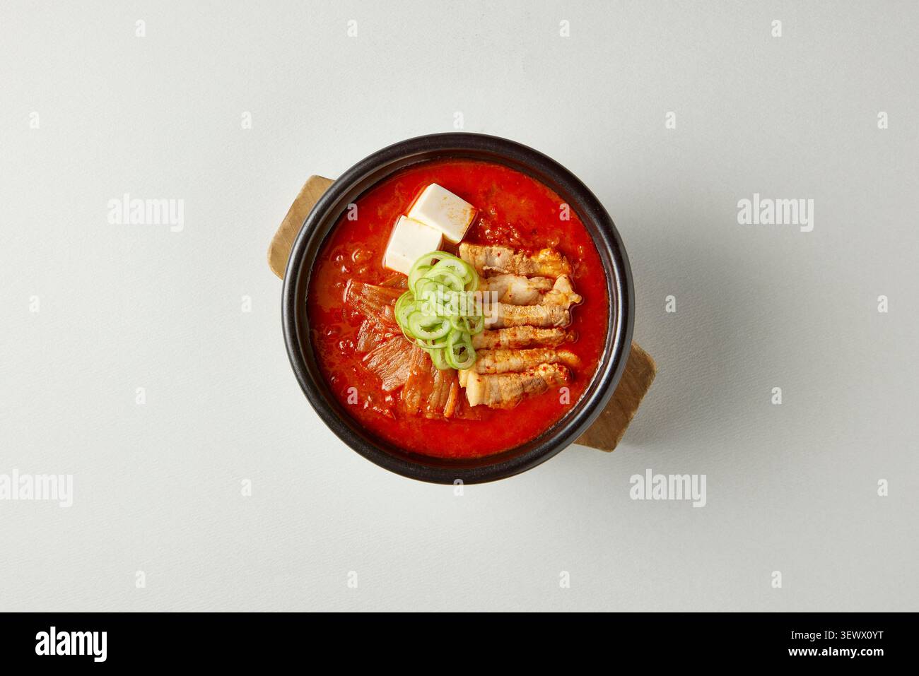 Stufato coreano di tofu sundubu jjigae servito in una tradizionale pentola nera di terracotta con tofu, kimchi e cipolla verde su sfondo grigio Foto Stock