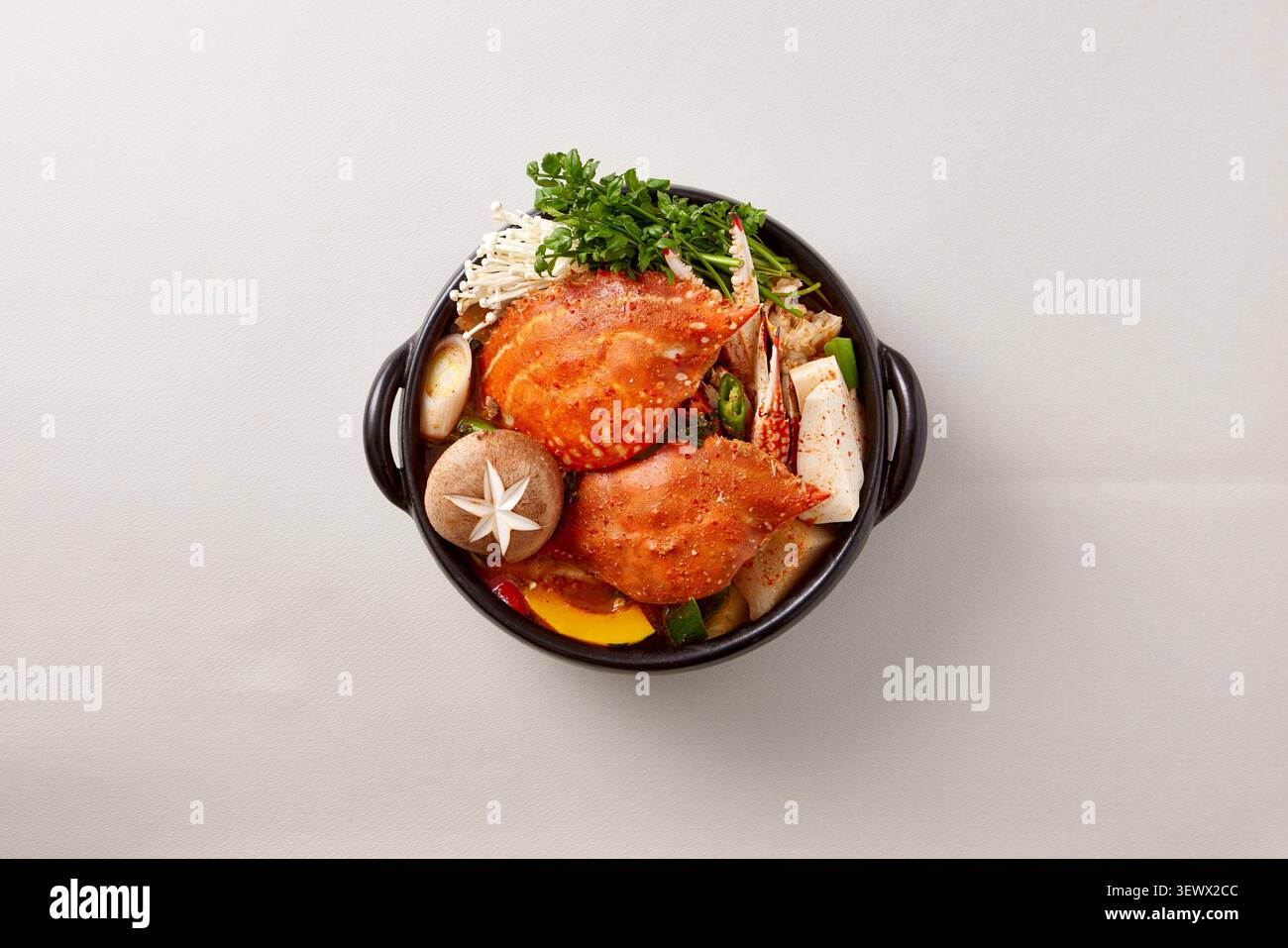 Pesce speziato coreano e piatto caldo di carne brasata serviti in una pentola nera di terracotta con granchio, abalone e verdure su sfondo grigio chiaro Foto Stock