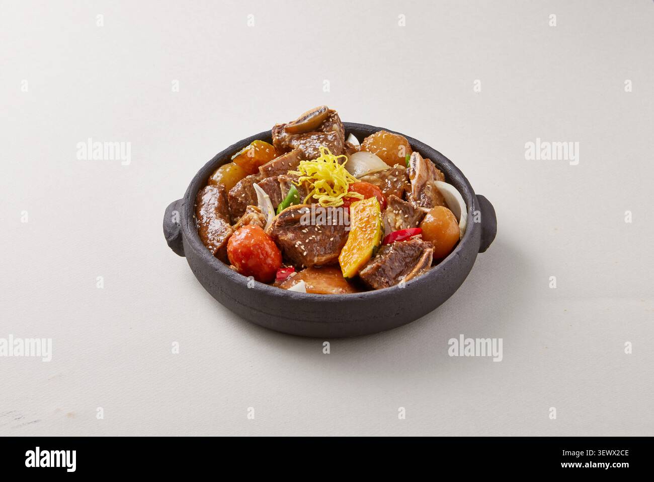 Pesce speziato coreano e piatto caldo di carne brasata serviti in una pentola nera di terracotta con granchio, abalone e verdure su sfondo grigio chiaro Foto Stock