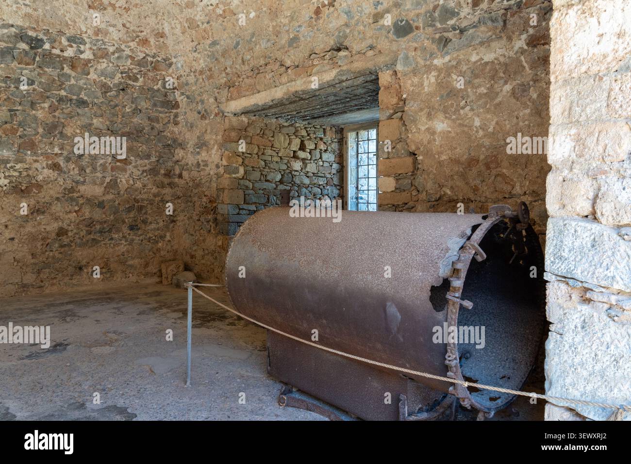 Grandi caldaie cilindriche in metallo arrugginito sono racchiuse da una barriera di corda all'interno di una stanza abbandonata in muratura di pietra sull'isola di Spinalonga. Foto Stock