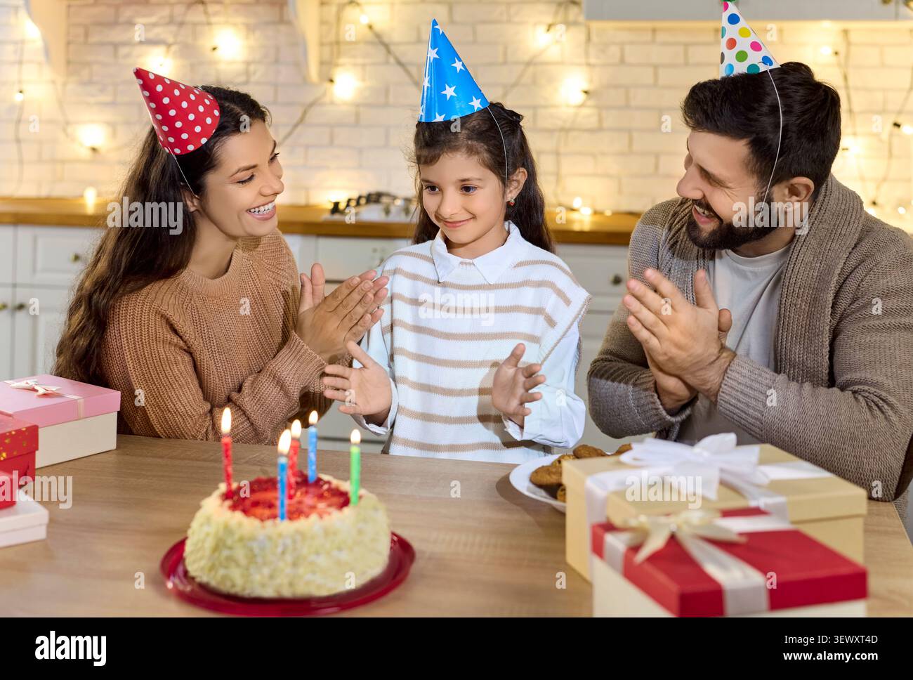 Genitori e figlia festeggiano il compleanno a casa con torta, candele, regali, gioia Foto Stock