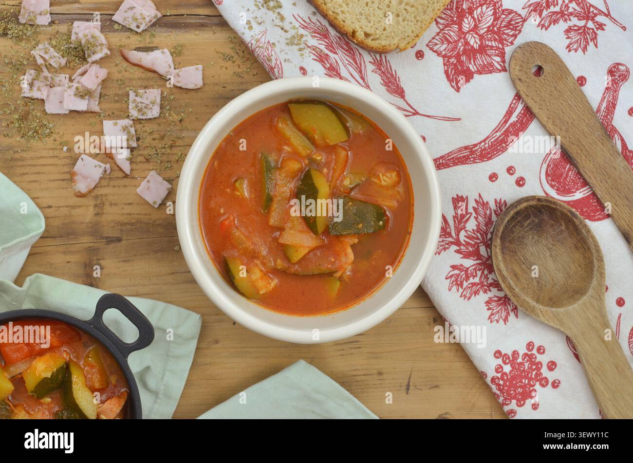 Pasto locale semplice: ​​ham a fette, lecho o zuppa con pezzi di verdure. Zucchine e salsa di pomodoro in un recipiente su un tavolo di legno. Foto Stock