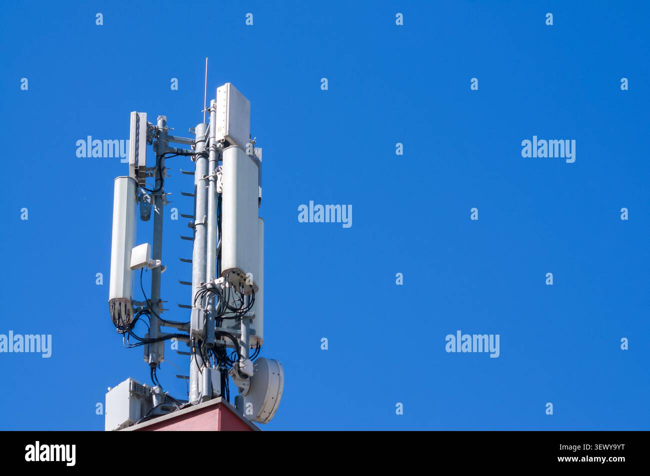 Vista ad angolo basso di una moderna torre di telecomunicazione con antenne cellulari 5G e 4G su uno sfondo blu chiaro del cielo estivo. Rete di telefonia mobile i Foto Stock