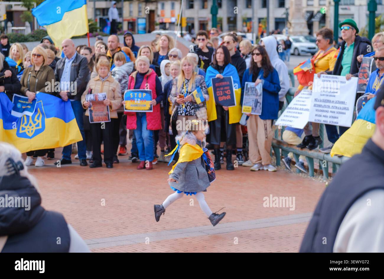 Dimostrazione con persone che tengono bandiere e cartelli ucraini, incluso un cartello "STOP" prominente. Un bambino avvolto nella bandiera gialla e blu Foto Stock
