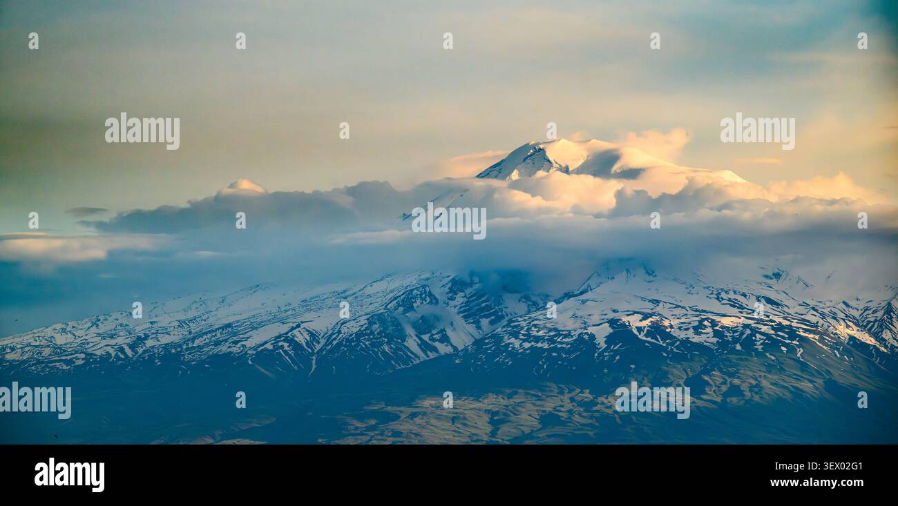 Le cime innevate si innalzano sopra nuvole nebbiose. La luce soffusa si illumina su creste distanti Foto Stock