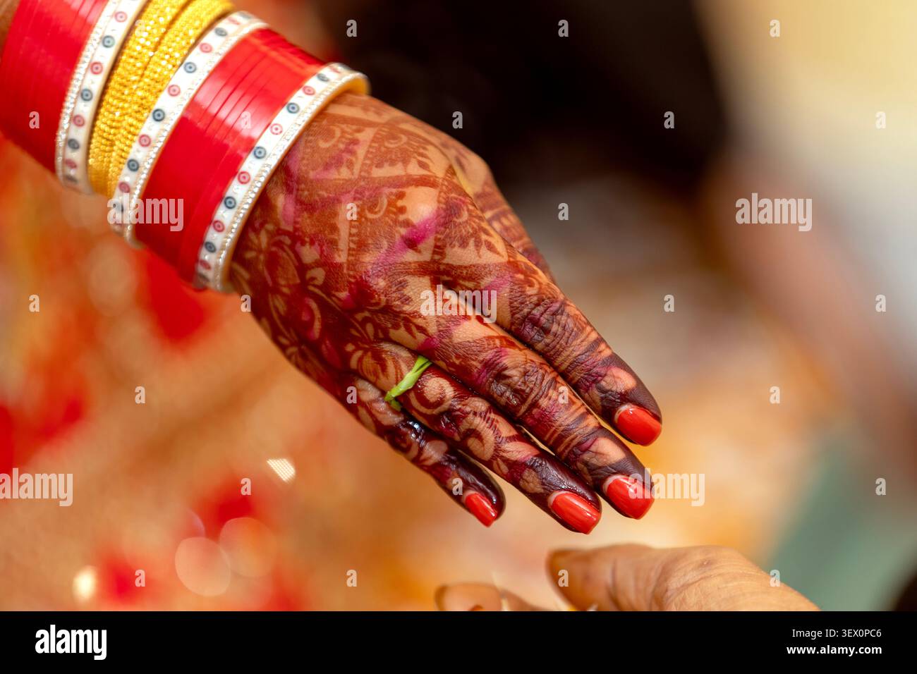 La mano della sposa indiana adornata di henné e bracciali, pronta per un rituale Foto Stock