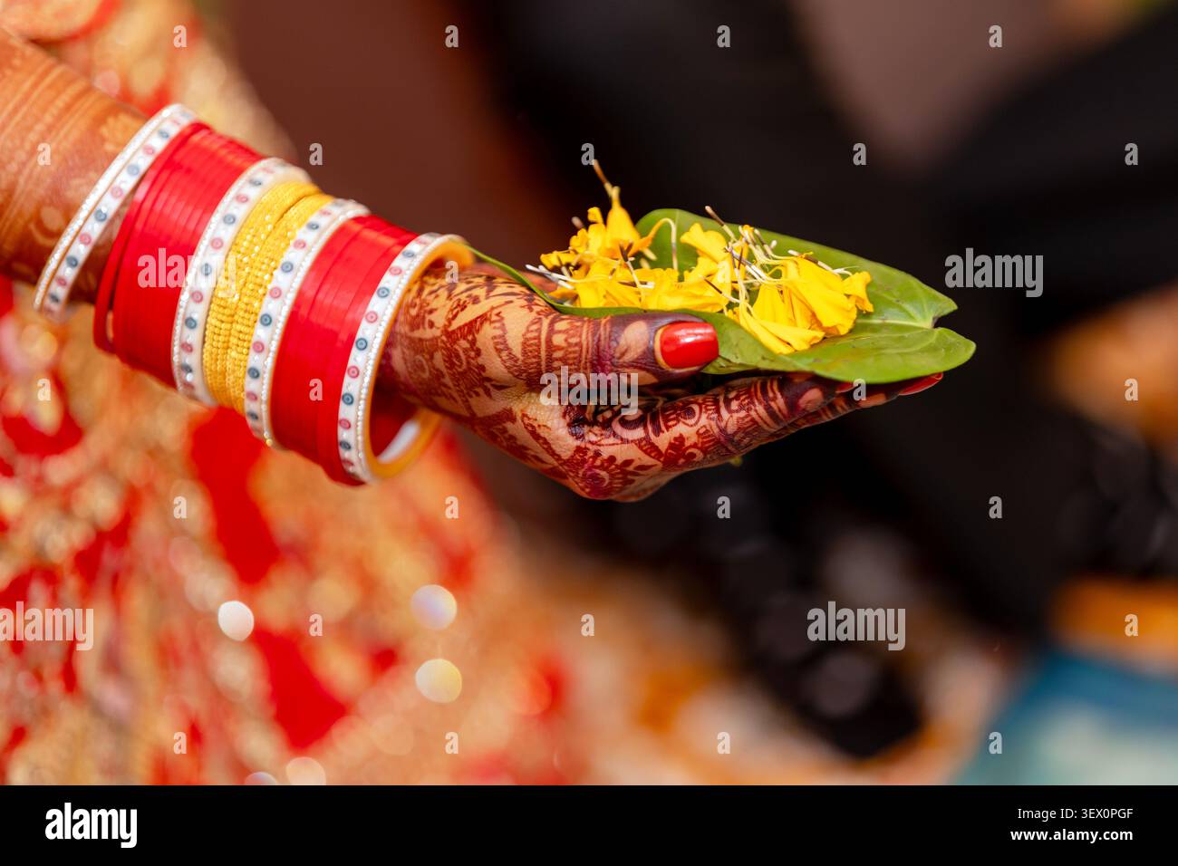 La mano decorata della sposa indiana regge una foglia di betel di buon auspicio con petali di fiori gialli Foto Stock