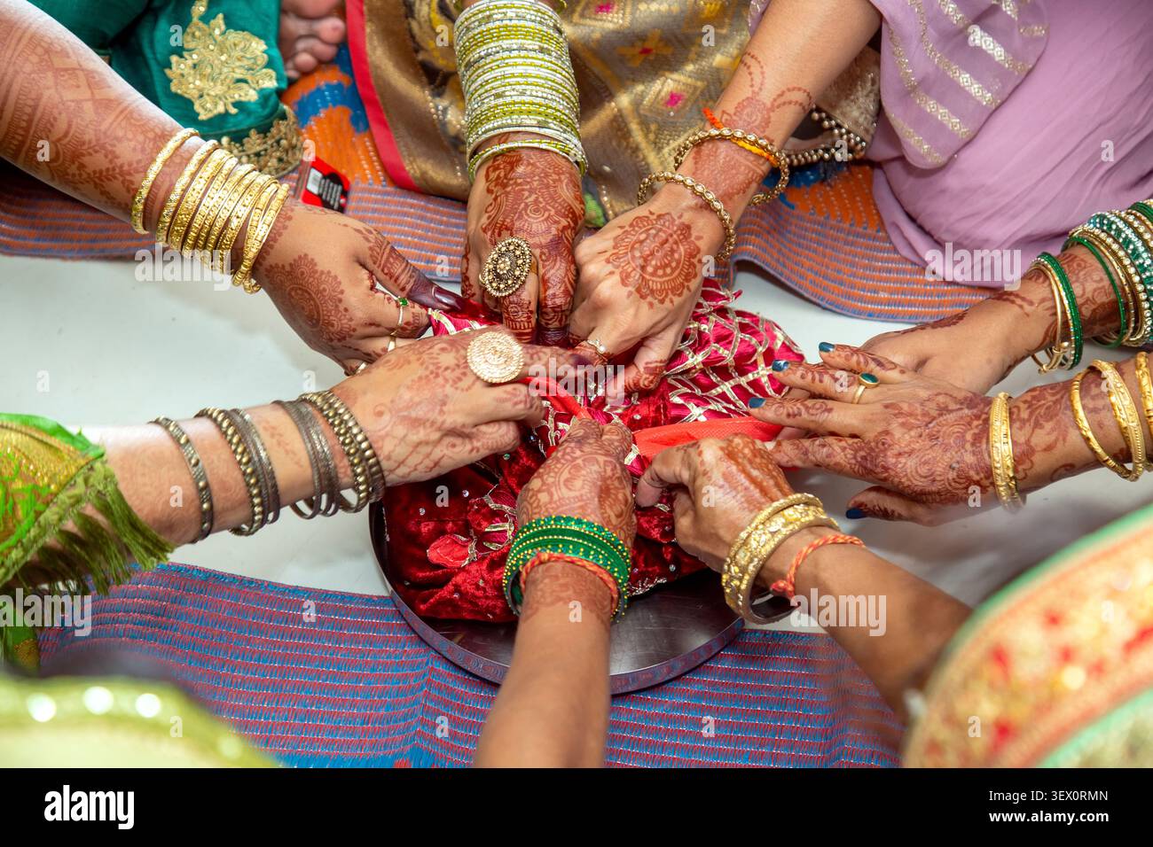 Un gruppo di donne adornate da elaborati schemi mehndi e bracciali colorati si riuniscono per svolgere un compito ritualistico, simboleggiando l'unità e l'heri culturale Foto Stock