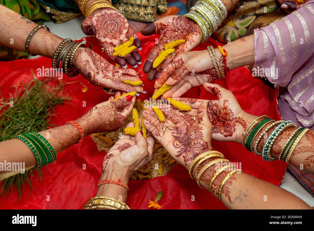 Un gruppo di donne con mani splendidamente decorate partecipa a un rituale culturale, tenendo pezzi di curcuma di colore giallo brillante Foto Stock