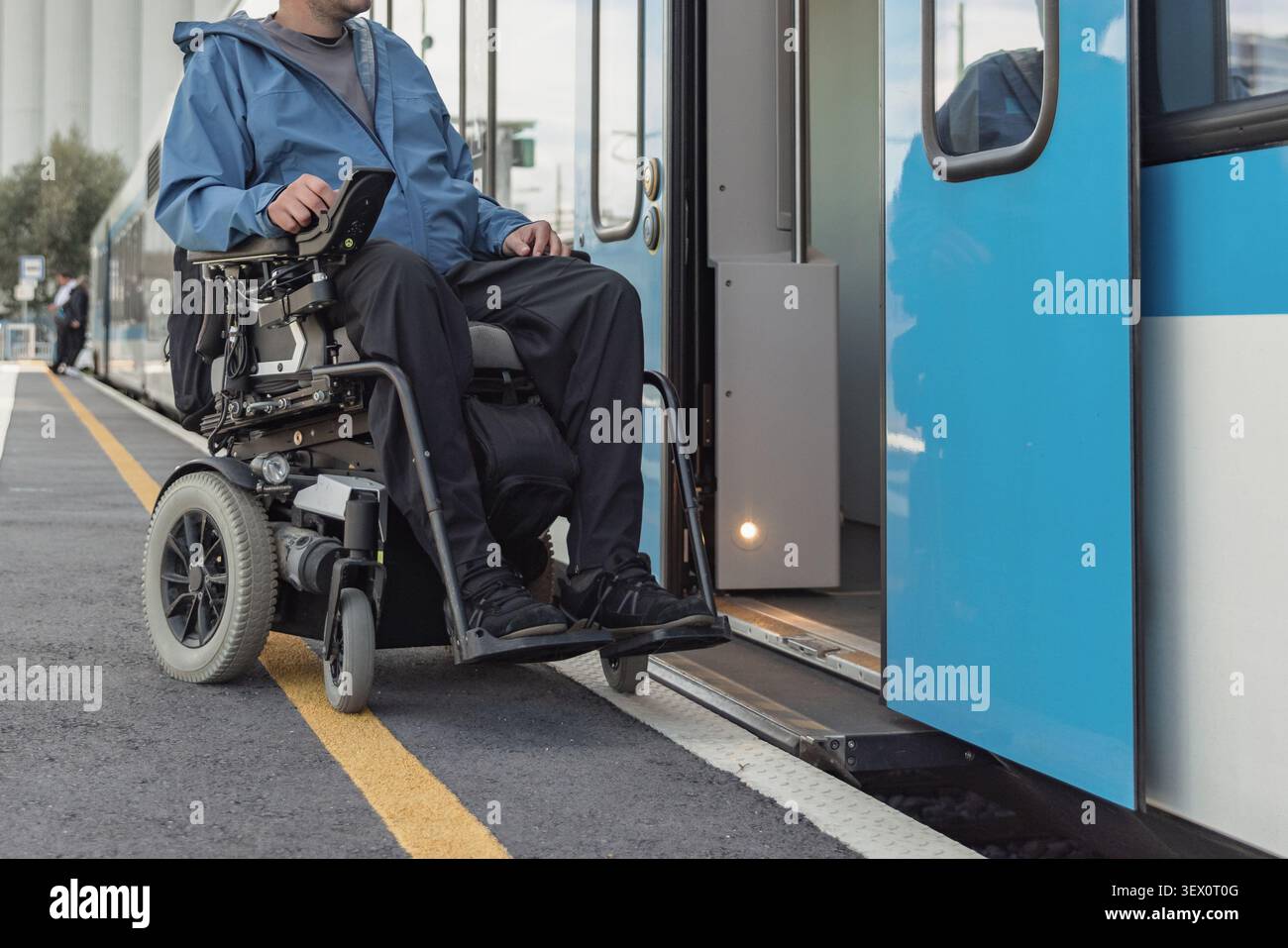 La persona con disabilità utilizza una sedia a rotelle per salire a bordo di un treno in una stazione, mostrando il trasporto accessibile per tutti. Foto Stock