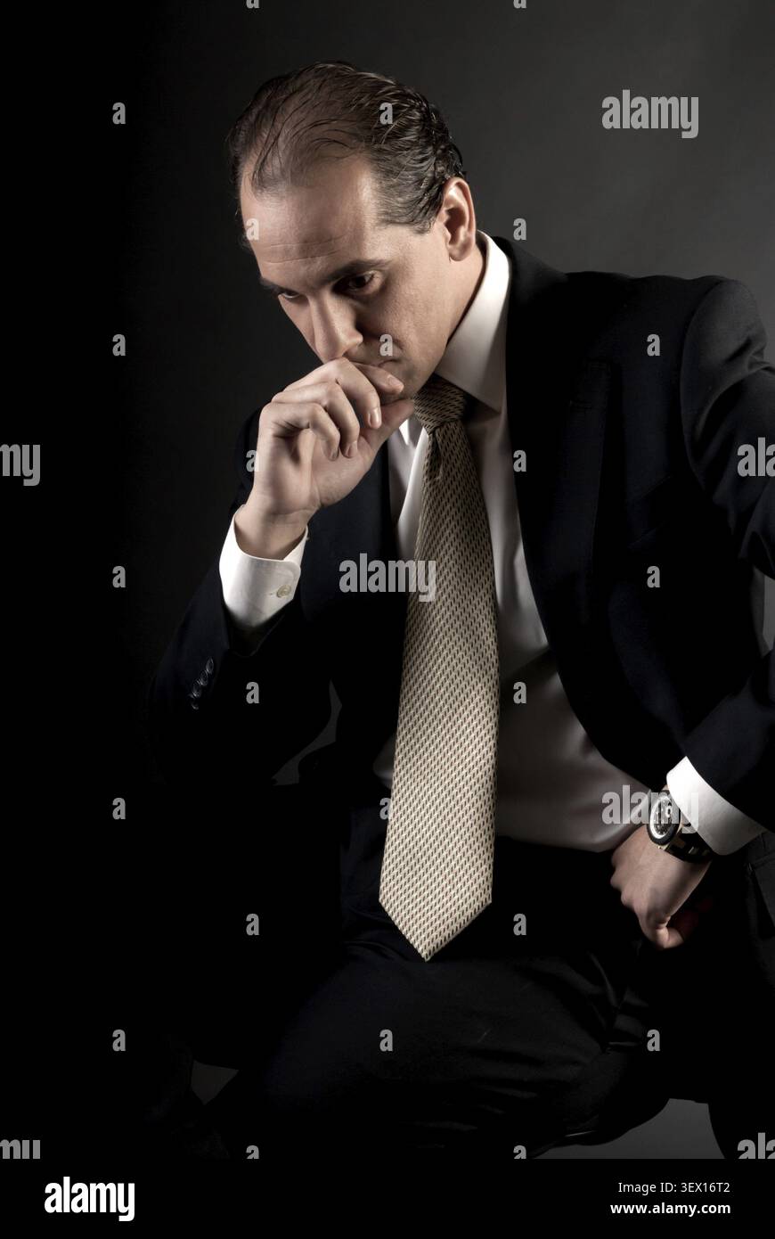 Uomo d'affari adulto pensa seriamente seduto su sfondo scuro Foto Stock