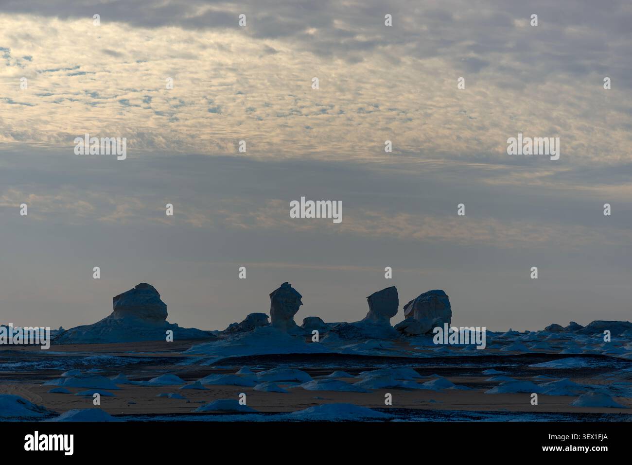 Mound di gesso bianco brillano sotto la luce del crepuscolo con rocce scolpite in lontananza, Deserto Bianco, Egitto Foto Stock