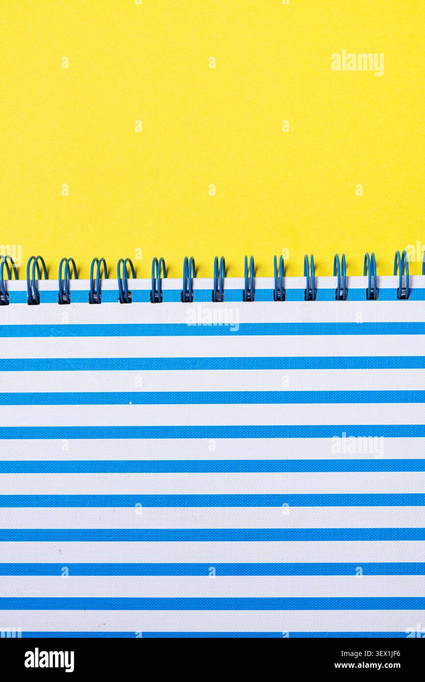 Sfondo giallo brillante con taccuino a righe orizzontali e rilegatura a spirale blu Foto Stock