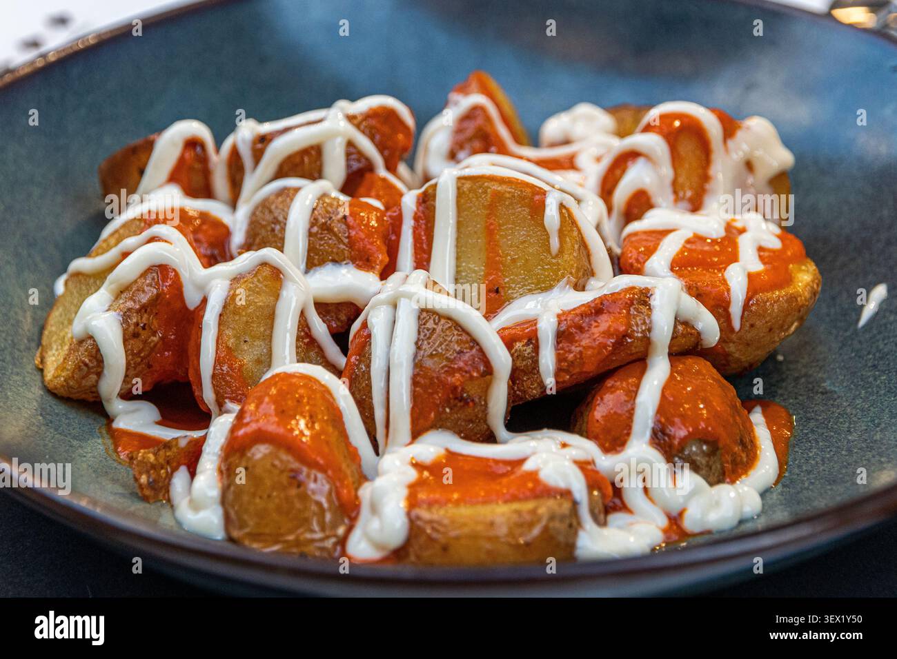 Spagna. Patatas bravas, patate fritte a spicchi condite con salsa brava piccante e aioli all'aglio, una classica tapa servita su un piatto di ceramica scura Foto Stock