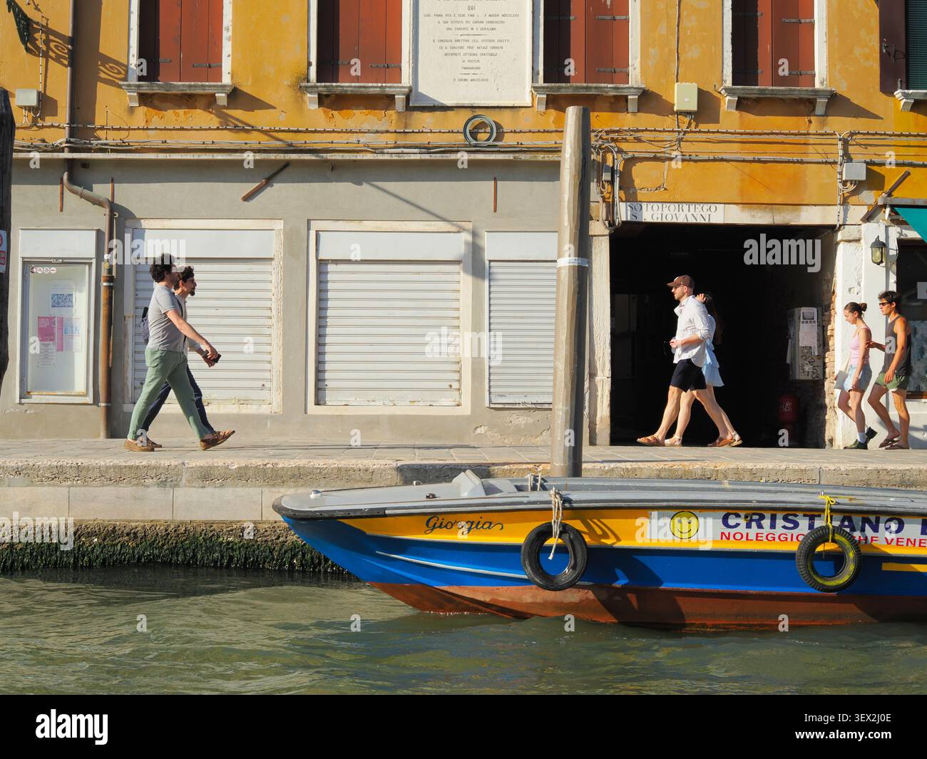 Venezia, Italia - 29 maggio 2026: Persone che camminano lungo una strada sul canale di Venezia con una barca colorata ormeggiata in primo piano Foto Stock