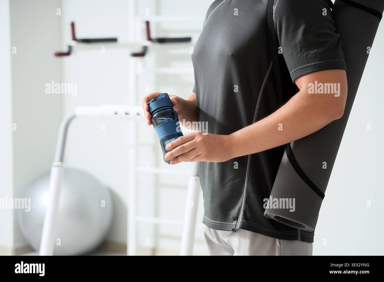 Uomo sportivo con bottiglia d'acqua e materassino fitness in palestra Foto Stock