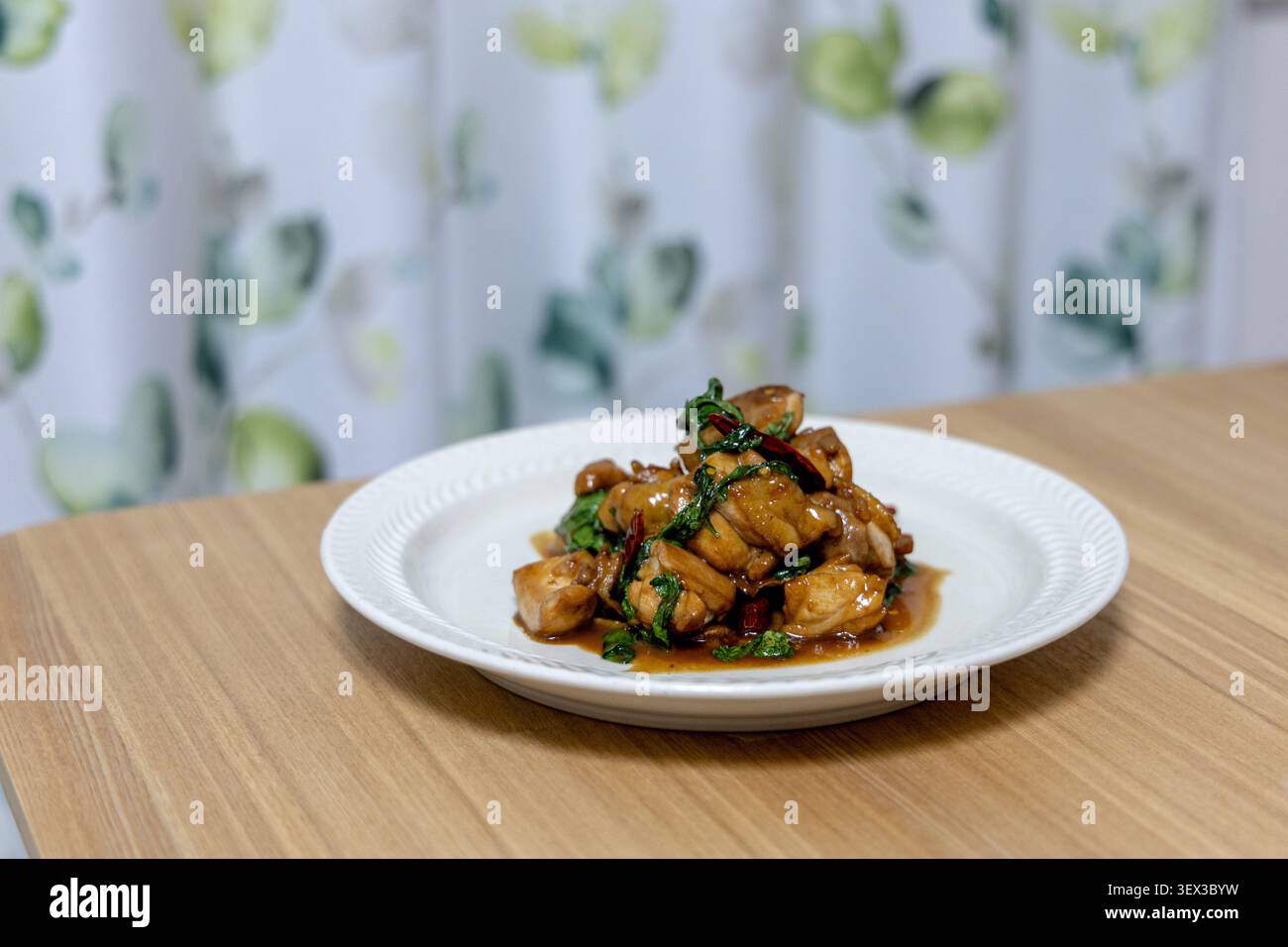 Un piatto di tre tazze di pollo si siede su un tavolo da pranzo in legno, i pezzi di pollo brasati glassati in ricca salsa di soia e sesamo con profumate foglie di basilico e peperoncino secco. Un classico piatto cinese casalingo servito a cena di famiglia. Foto Stock