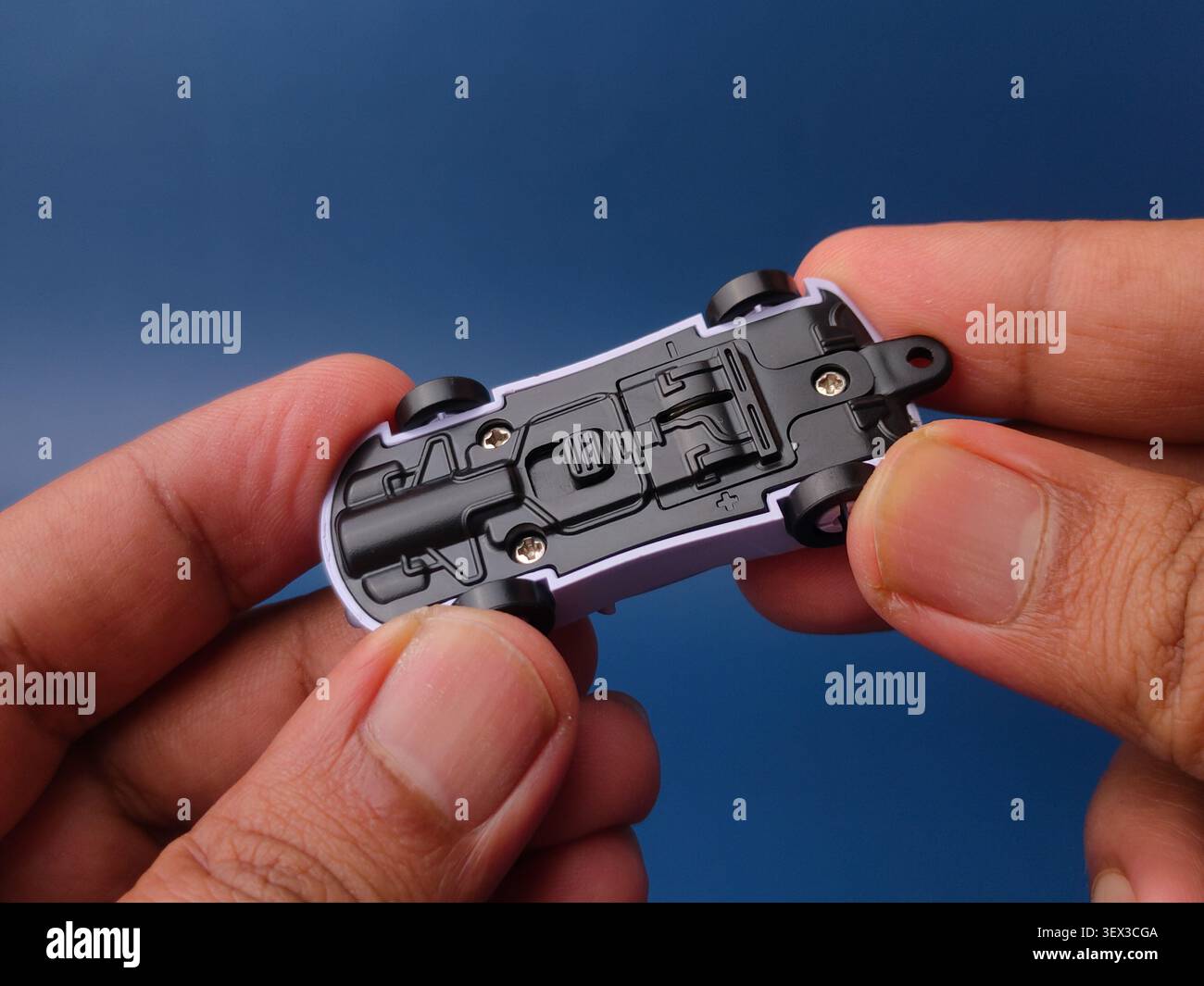 Due mani reggono un piccolo modello di auto giocattolo in plastica rovesciata, che mostra il suo sottocarro nero con viti argentate. Foto Stock