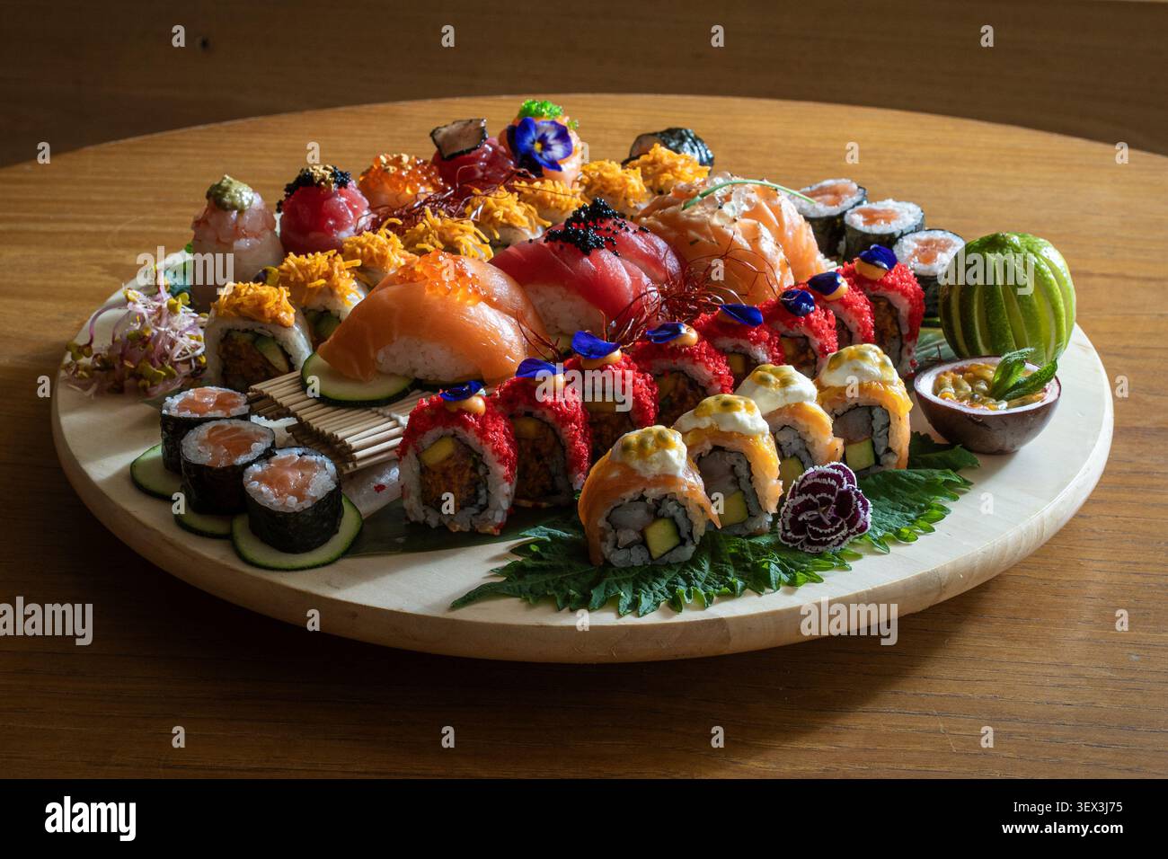 Un piatto di sushi splendidamente organizzato con una varietà di panini e nigiri su una superficie rotonda in legno. Foto Stock