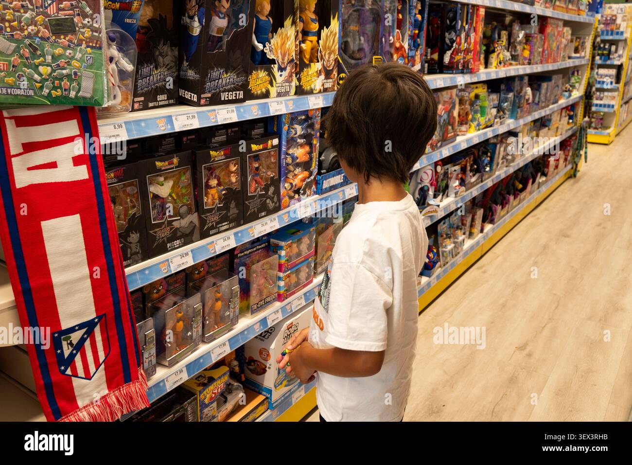 Bambino che guarda le action figure sugli scaffali in un negozio di giocattoli illuminato. Giugno 27 2026 Foto Stock