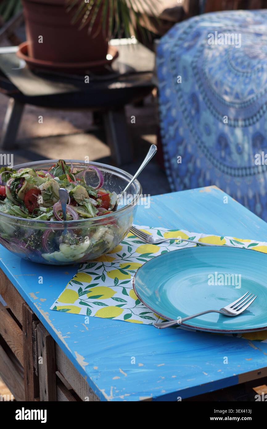 Insalata mista fresca su un tavolo rustico all'aperto con piatto blu vuoto in un accogliente ambiente da pranzo in giardino Foto Stock