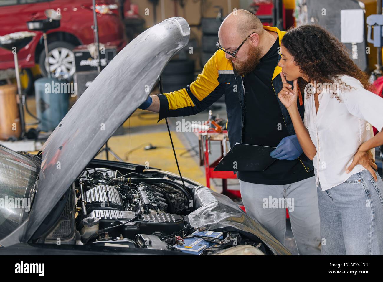 Assistenza motore auto in officina, il cliente si preoccupa di parlare con il tecnico meccanico. Durante il servizio auto in officina, servizio auto Foto Stock