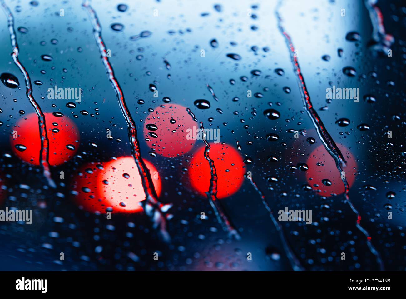 Pioggia bagnata umida, sfocatura bokeh Night cool chill background, stagione delle piogge, pioggia sul parabrezza traffico stradale con tonalità di colore rosso azzurro. Foto Stock