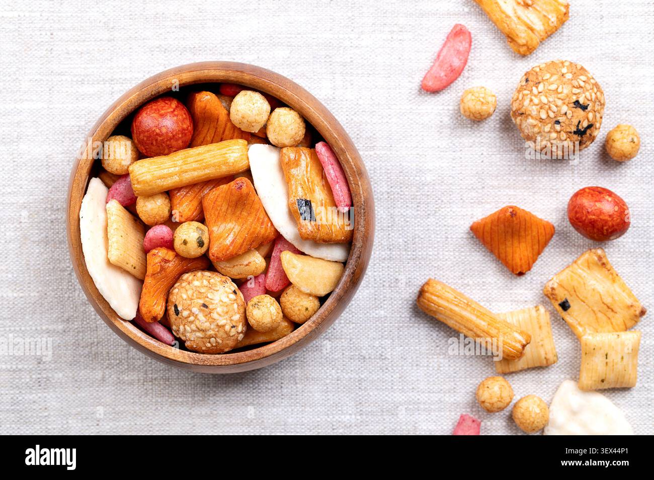 Mix giapponese, cracker di riso giapponese e arachidi ricoperte in ciotola di legno su lino. Cracker a base di riso al forno e farina di grano. Foto Stock