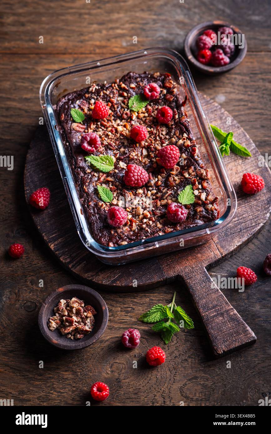Decadente brownie al lampone al cioccolato cotto in piatto di vetro, condito con noci e menta Foto Stock