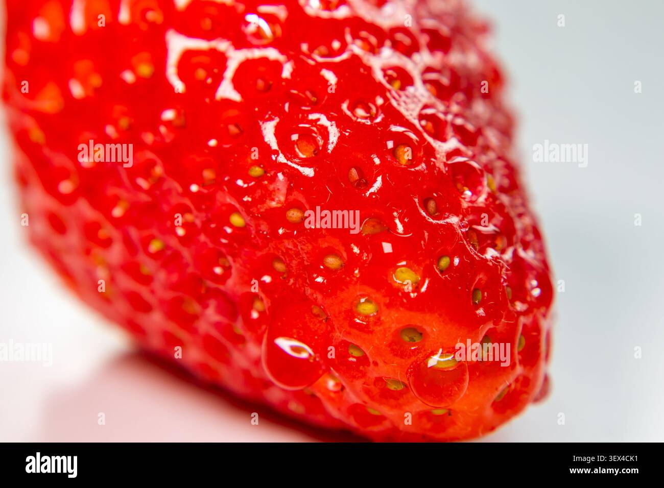 Primo piano della pelle di fragola che rivela una lucentezza lucida e semi sparsi su un morbido sfondo liscio Foto Stock