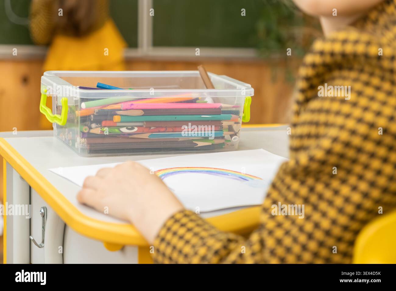 Un bambino crea un progetto artistico presso una scrivania in legno con un contenitore di strumenti di scrittura nelle vicinanze per rappresentare l'apprendimento creativo e il pri Foto Stock