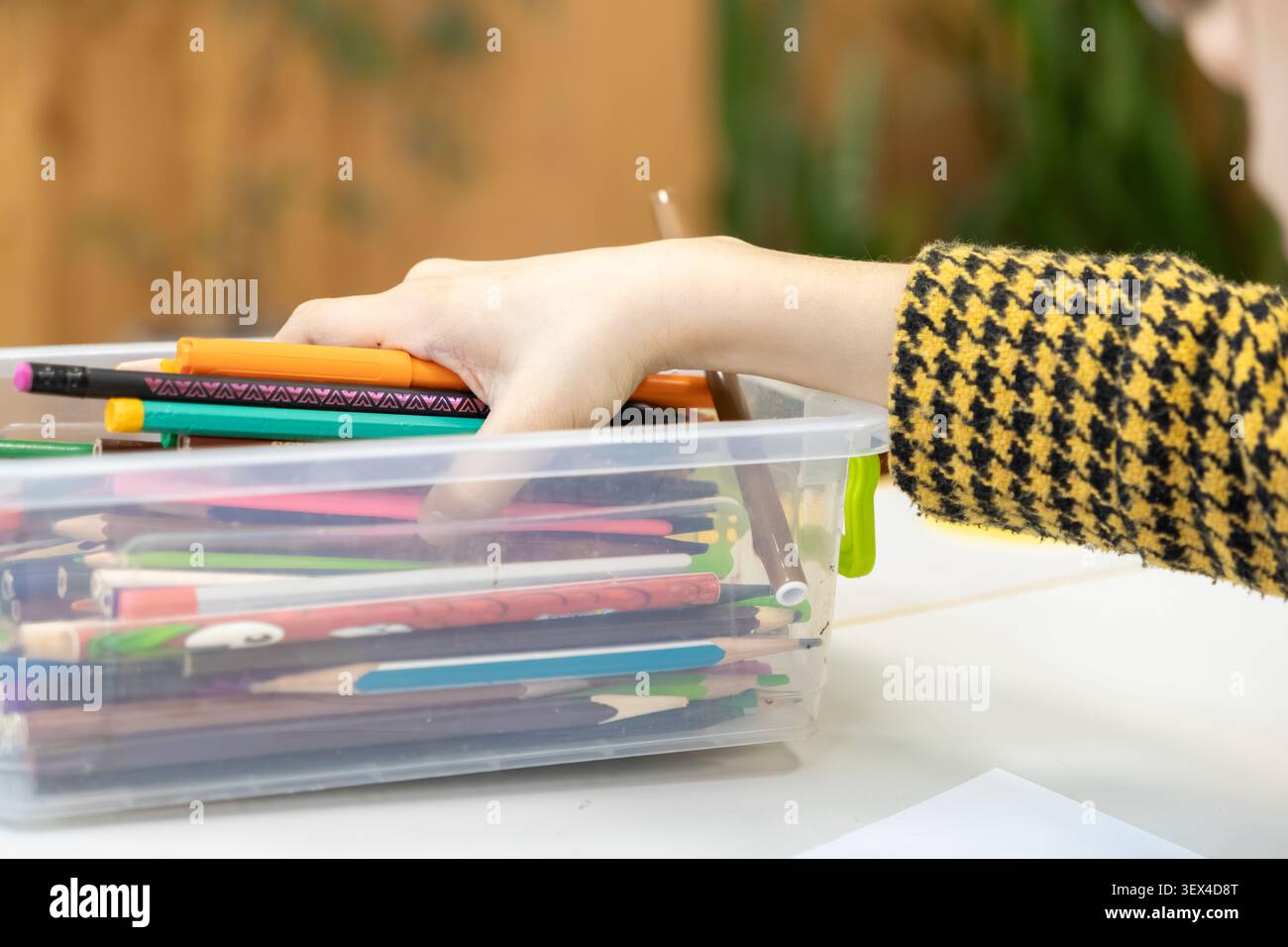 Una persona cerca una penna colorata all'interno di una scatola trasparente piena di strumenti di disegno assortiti per simboleggiare la preparazione artistica e un crea organizzato Foto Stock