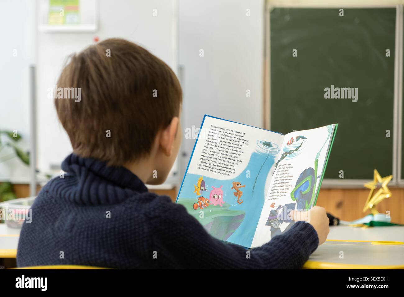 Kiev, Ucraina - 21 marzo 2026: Uno studente viene assorbito in un libro colorato durante una tranquilla sessione scolastica, illustrando la sua curiosità e il gro Foto Stock