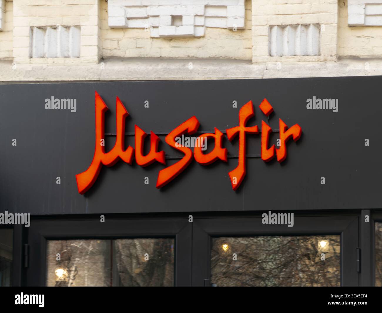 Kiev, Ucraina - 21 marzo 2026: Cartellonistica Musafir con lettere rosse stilizzate su uno sfondo nero sopra una porta d'ingresso di vetro in una trafficata metropolita Foto Stock