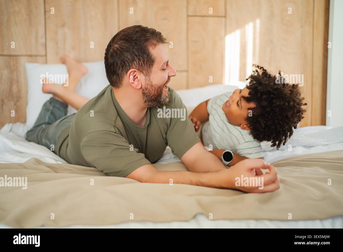 Padre e figlio sdraiati a letto, trascorrendo del tempo insieme e ridendo Foto Stock