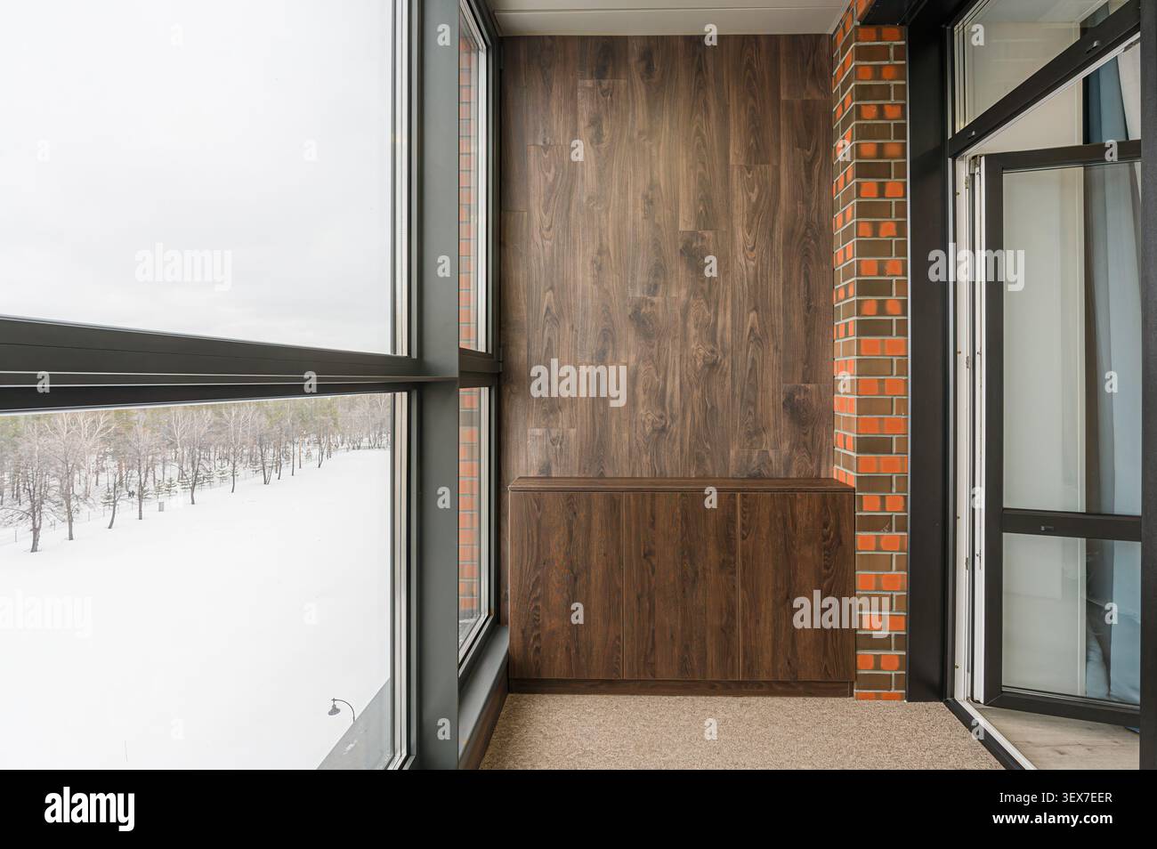 balcone moderno con pannelli in legno, accenti in mattoni e una grande finestra che si affaccia su un paesaggio innevato Foto Stock