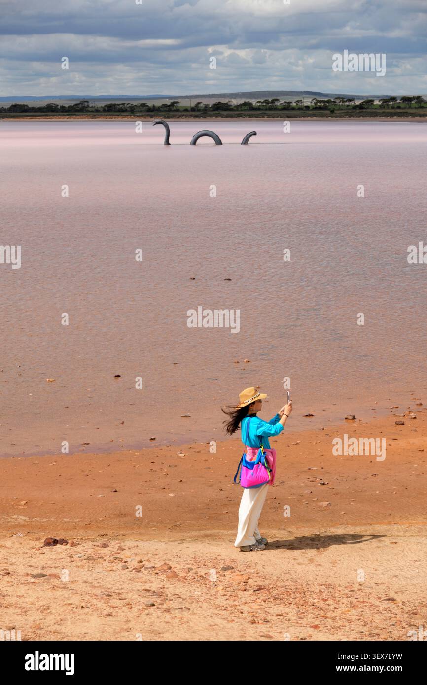 Australia, Australia meridionale, Lochiel, Lake Bumbunga o Pink Lake, turisti che scattano una foto al lago salato rosa con la scultura Loch-Eel Monster, ispirata al mostro di Loch Ness, sullo sfondo Foto Stock