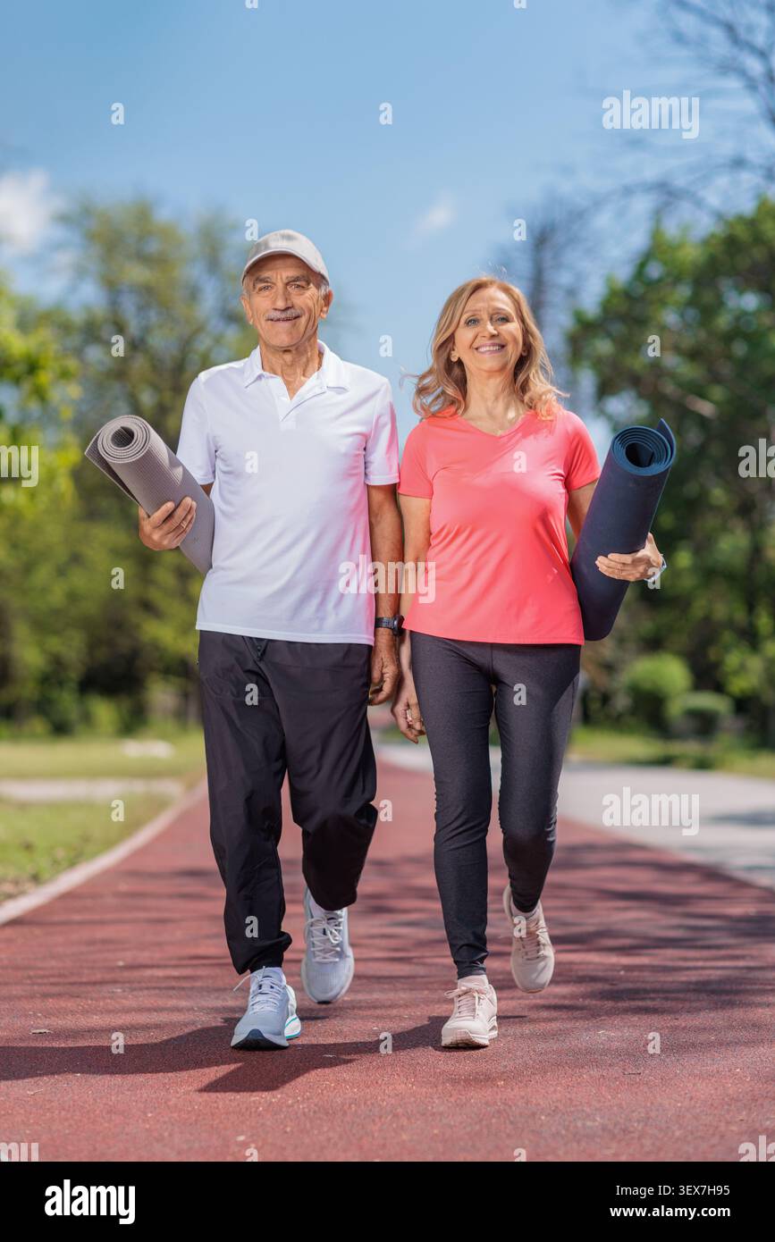 Una coppia matura attiva che cammina in un parco con materassini fitness Foto Stock