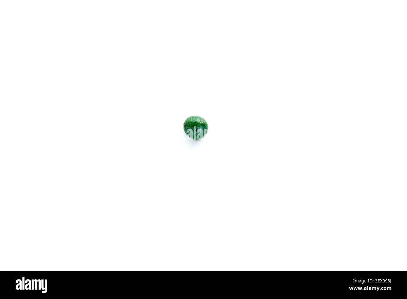 Un seme di ortaggi rivestito su sfondo bianco pulito. Un solo seme di cavolo verde trattato posto al centro Foto Stock