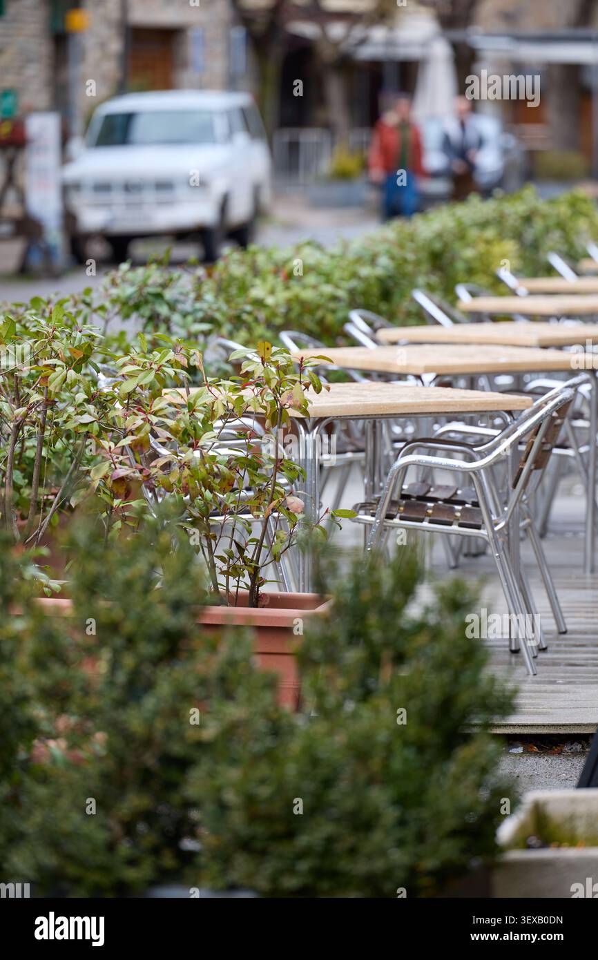 Tavoli e sedie vuoti da caffè all'aperto fiancheggiati da piante in una strada tranquilla in una città europea Foto Stock