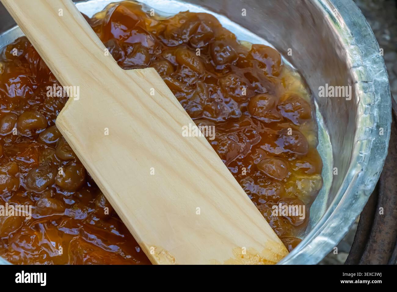 Primo piano della marmellata di ciliegie gialle fatta in casa in una pentola di metallo con una paletta di legno, catturando il tradizionale processo di conservazione e l'autentica stagione Foto Stock