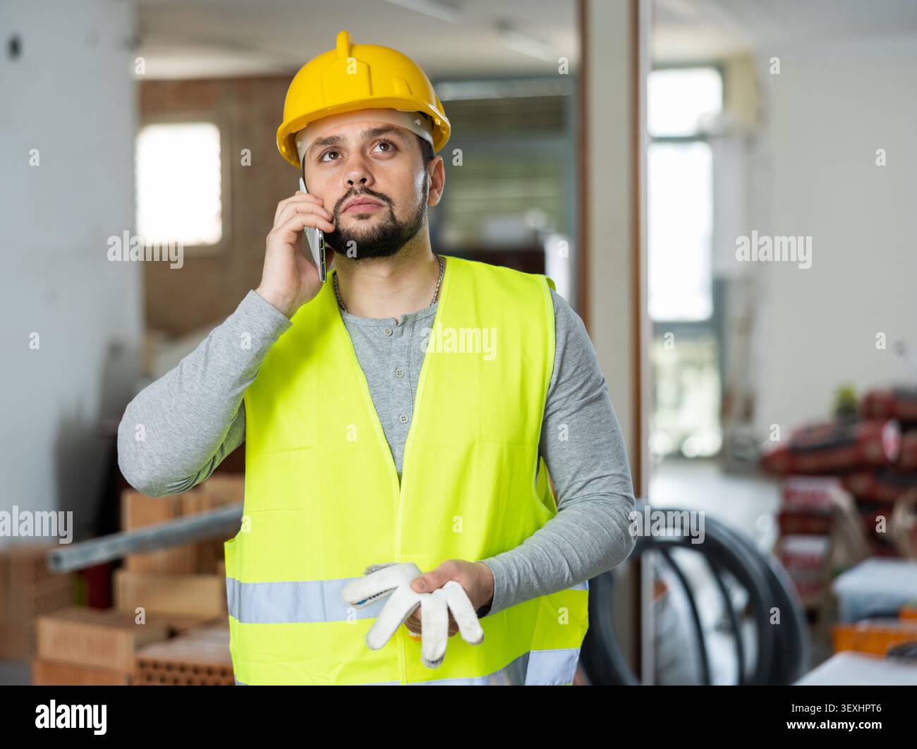 Giovane ingegnere civile bearded che parla al telefono in cantiere Foto Stock