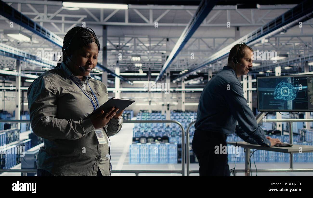L'amministratore di sistema afroamericano utilizza l'intelligenza artificiale su un tablet in una server farm per aiutare i clienti a risolvere i problemi di hosting del sito Web. Foto Stock