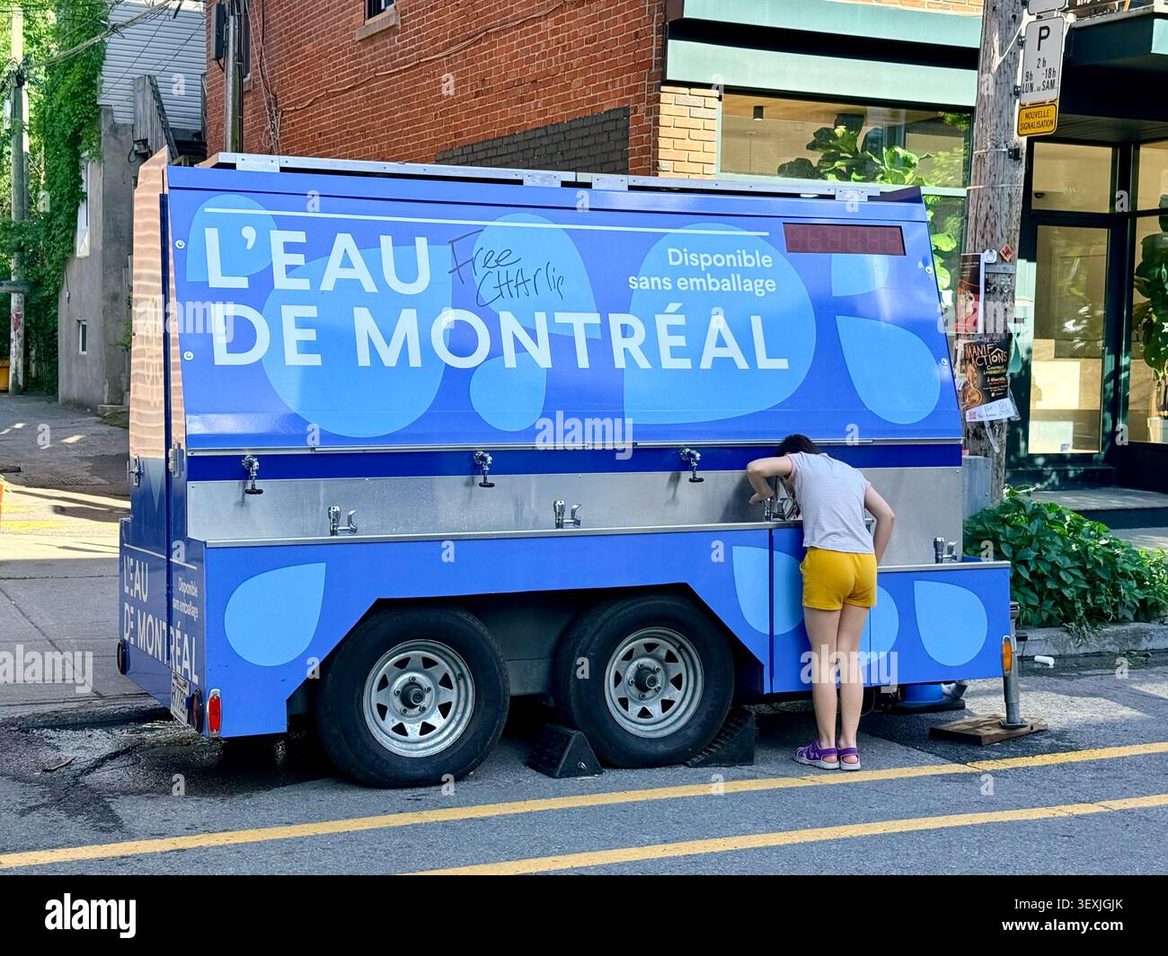 Una persona utilizza una stazione mobile per l'acqua potabile l'Eau de Montréal a Villeray, Montreal, Quebec, Canada, promuovendo l'accesso pubblico all'acqua di rubinetto e ricaricando il cu - Immagine stock catturata con smartphone