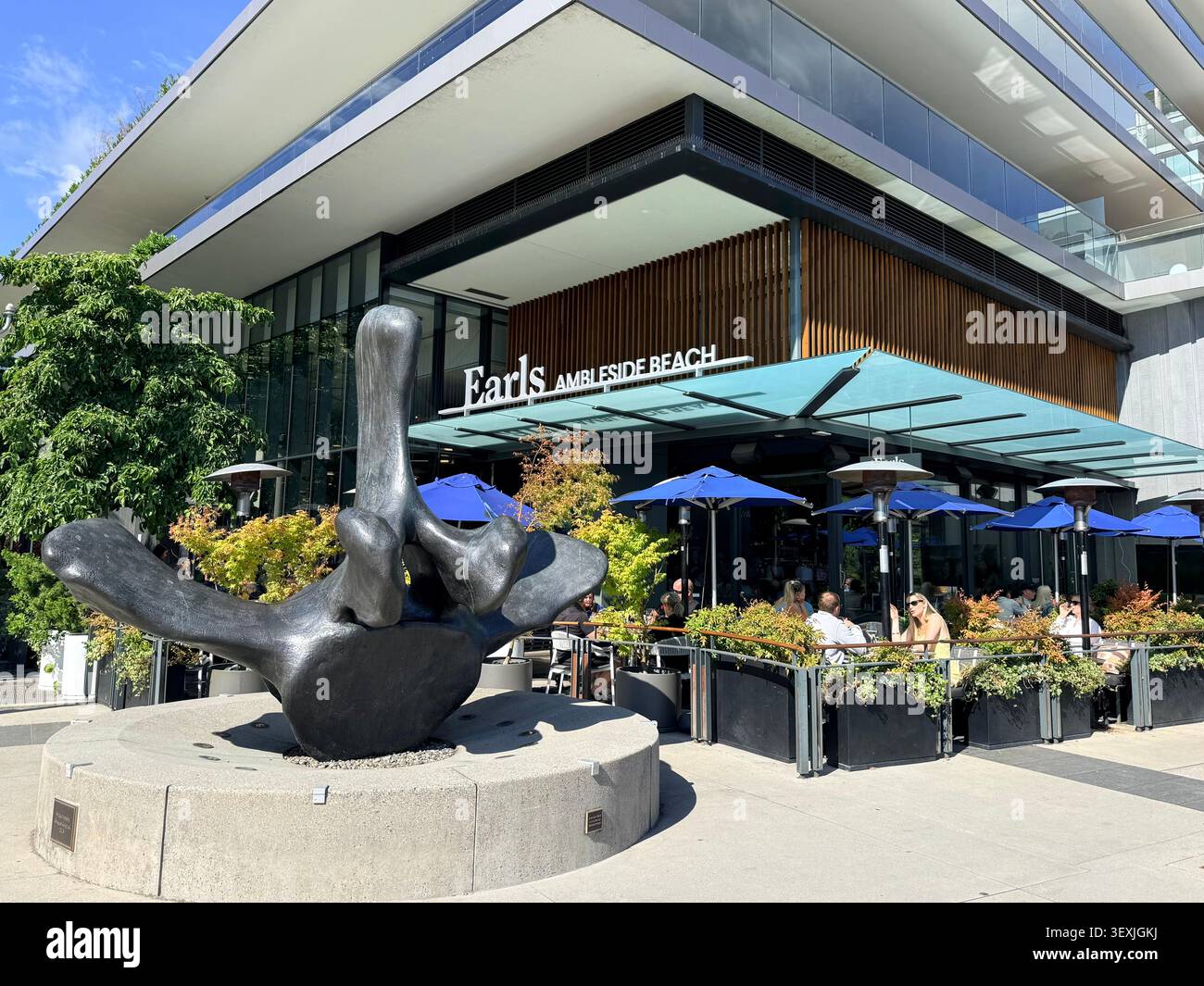 Patio del ristorante Earls Ambleside Beach con una grande scultura pubblica all'esterno di un moderno sviluppo sul lungomare a West Vancouver, British Columbia, Cana Foto Stock